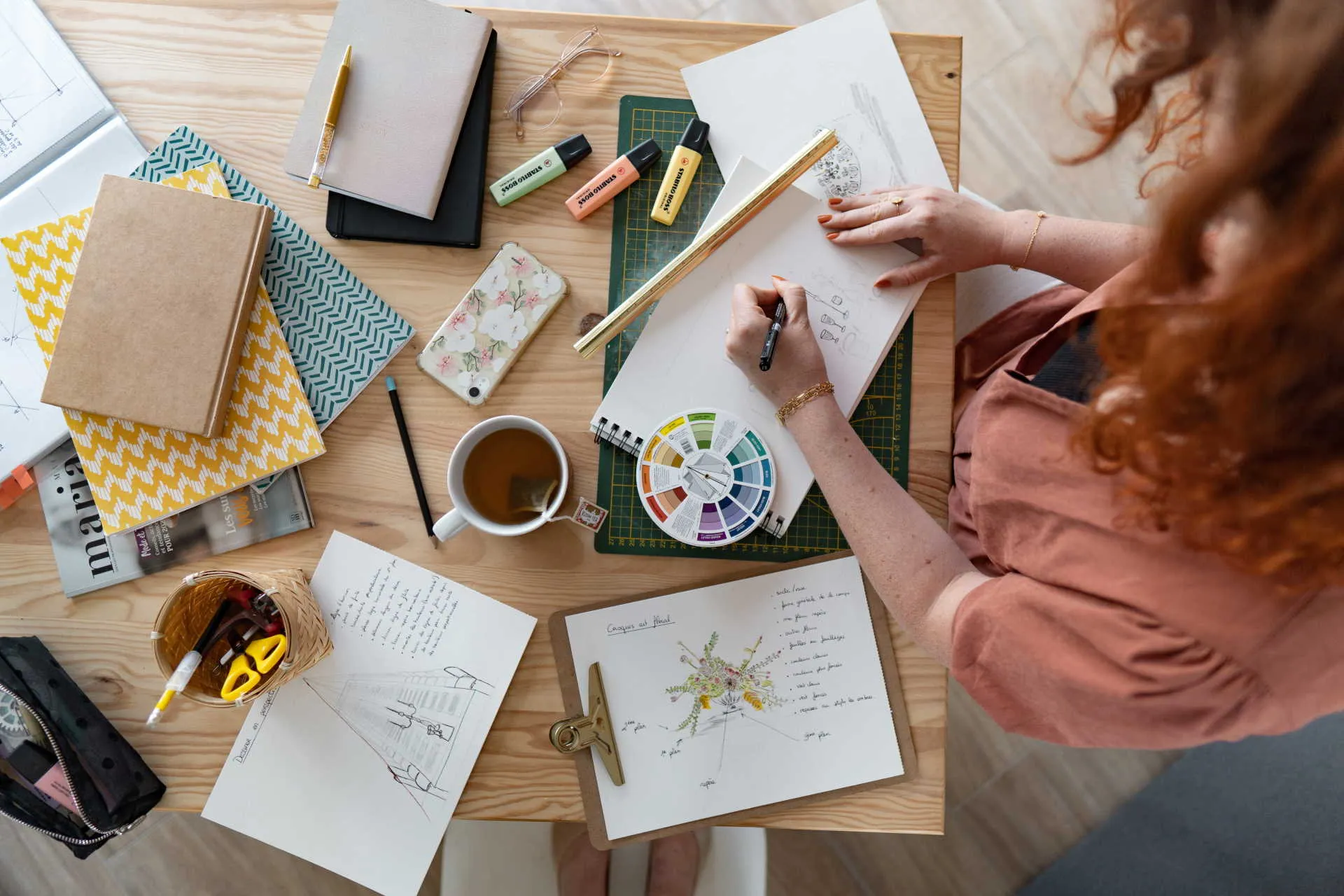 Cette photo représente Elorri la créatrice de Sourires d'Aubépine sur son bureau en train de faire un croquis d'un centre de table avec des bougies